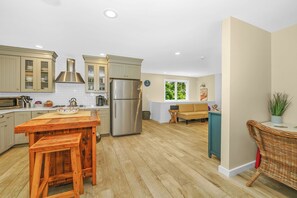 A modern kitchen with wooden bar stools, stainless steel appliances, and a view to the living area.