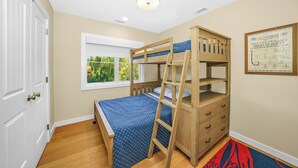 A bunk bed room with a window, a ladder, a dresser, and a chart on the wall.