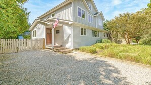 A two-story house with a front porch, a wooden fence, and a gravel driveway.