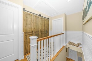 A hallway with a wooden door, white walls, a white railing, and a small shelf with decorative items.