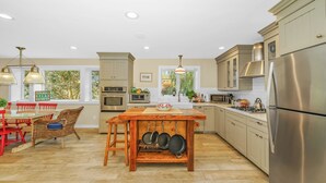 A modern kitchen with stainless steel appliances, a dining area with a wooden table, and a view of greenery outside.