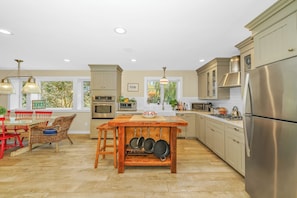 A modern kitchen with stainless steel appliances, a dining area with a wooden table, and a view of greenery outside. - 5 bdrm with pool - walk to the Harbor (Montauk)