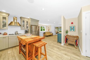 Een moderne keuken met een centraal eiland, roestvrijstalen apparatuur en een eethoek met een rieten stoel.