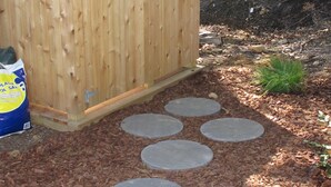 A wooden shed with a metal latch, surrounded by mulch and stepping stones.
