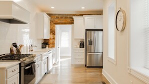 A modern kitchen with white cabinetry, a stainless steel refrigerator, and a brick accent wall.