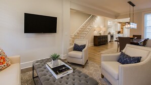 A spacious living room with a flat-screen TV, a comfortable sofa, a coffee table with a tray, and a staircase leading to the upper floor.