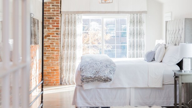 A bedroom with a large bed, a white rug, and a brick wall.