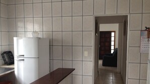 A kitchen with white tiled walls, a wooden countertop, a white refrigerator, and a visible door leading to another room.