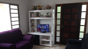 A living room with a purple sofa, a black sofa, a white entertainment unit with a TV, and a wooden door.