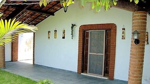 A covered outdoor area with a tiled floor, a door with a decorative panel, and a small garden with a palm tree.