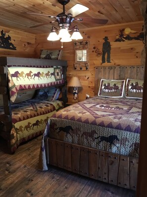 A rustic cabin bedroom with wooden walls, a ceiling fan, a bed with a horse-patterned quilt, and a nightstand with a lamp. - Wilderness Retreat Cabin- Lg Game Room, Private Hot Tub; 1 Mile to Thunder Ridge (Ridgedale)