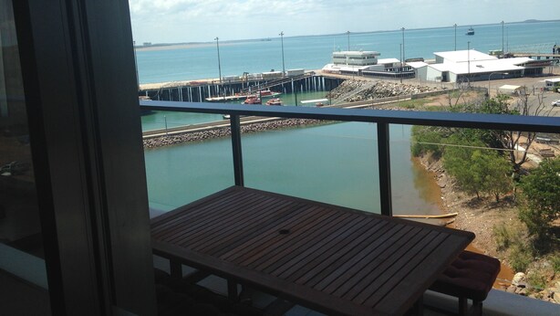 A balcony with a wooden table and a view of a coastal area with a pier and buildings. - Views of Darwin Harbor (Darwin City)