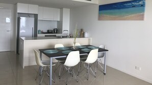 A modern kitchen with white cabinets, a stainless steel refrigerator, and a dining area with a black table and white chairs. - Views of Darwin Harbor (Darwin City)