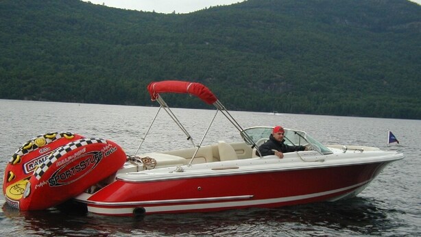 Un bateau à moteur rouge et blanc, doté d’un auvent, sur un lac paisible, entouré de collines verdoyantes.