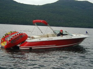 Un bateau à moteur rouge et blanc, doté d’un auvent, sur un lac paisible, entouré de collines verdoyantes.