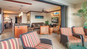 A spacious living area with wicker furniture, a glass coffee table, and a dining area with a wooden table and chairs.