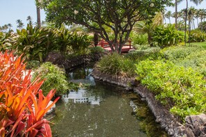 Ein ruhiger Garten mit einem kleinen Teich, üppigem Grün und einer roten Brücke.