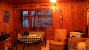 Un interior de cabaña acogedor con una mesa de comedor, sillas, un sillón de cuero, un sofá y una mesita de noche con una lámpara.