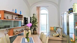 Een moderne woonkamer met een eethoek, een bank, een grote potplant en uitzicht op de omgeving via een boogvormige deuropening.