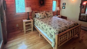 A wooden cabin bedroom with a bed, two bedside lamps, a ceiling fan, and two windows. - Bright cabin retreat happily situated 7 miles from Whiteface Mt (Jay)