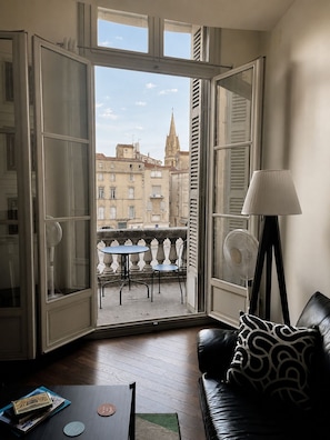 A room with a balcony, a table, a chair, a sofa, and a lamp. - Stylish, modern apartment in the historic centre of Montpellier. (Montpellier)