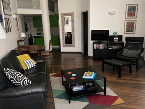 Un salon moderne avec un canapé en cuir noir, une table basse avec des livres, un téléviseur et une bibliothèque.