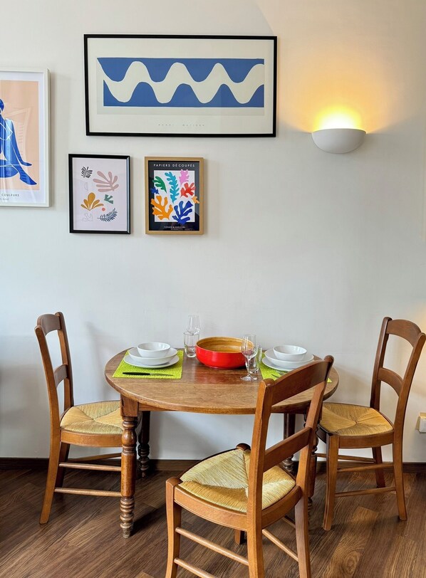 A dining area with a round wooden table, four wooden chairs with woven seats, and a wall-mounted light fixture. - Stylish, modern apartment in the historic centre of Montpellier. (Montpellier)