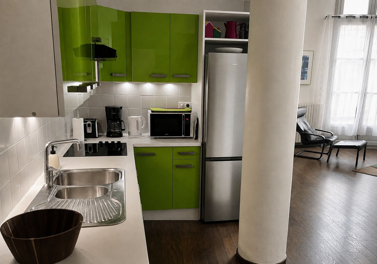 Une cuisine moderne avec des meubles de couleur verte, un réfrigérateur en acier inoxydable, un four à micro-ondes et une machine à café.