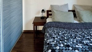Una camera d'albergo con un letto, un comodino, una foto incorniciata appesa al muro e una finestra con persiana chiusa.