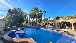 A swimming pool with a stone archway, surrounded by palm trees and a patio area with outdoor seating. - Castell Villa Bohío Mallorca (Lluchmajor)
