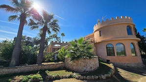 A castle-like building with a stone wall and palm trees. - Castell Villa Bohío Mallorca (Lluchmajor)
