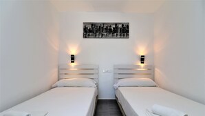 Camera d'albergo con due letti singoli, lenzuola bianche, un'opera d'arte con soggetto urbano sopra i letti e luci a parete su entrambi i lati.