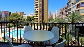 Un balcone con vista sulla piscina, circondato da palme e edifici urbani.