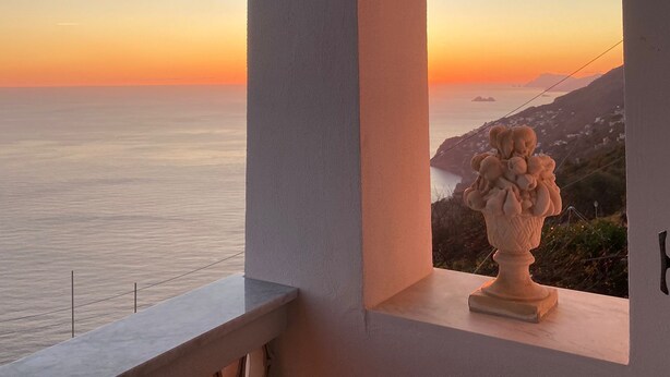 Un balcó amb vista al mar al capvespre, una paret blanca i una gerra decorativa.