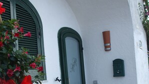 Un edifici blanc amb una porta verda, una test de flors vermella i una tanca de fusta amb flors.
