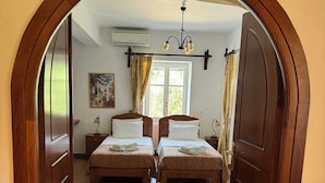 Quarto com duas camas, janela com cortinas, um quadro na parede e um candelabro.