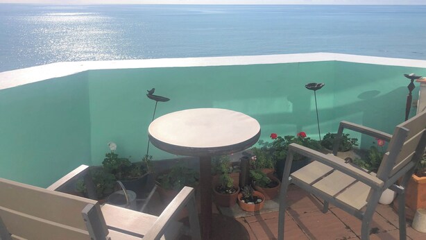 Ein Balkon mit Meerblick, einem runden Tisch und Topfpflanzen.
