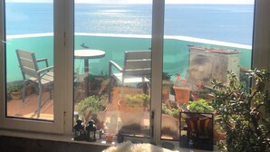 Ein Balkon mit Blick auf den Ozean, zwei Stühle, ein Tisch und Kübelpflanzen.
