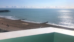 Ein Strand mit einem Pier, der sich ins Wasser erstreckt, einer Promenade am Ufer und einem wolkenlosen Himmel.