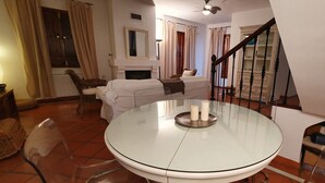 Een woonkamer met een ronde glazen tafel, een bank, een open haard en een trap.