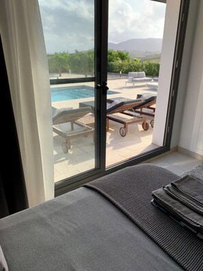 Une chambre avec vue sur une piscine et des chaises longues à l’extérieur.