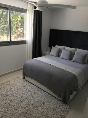 Ein Schlafzimmer mit einem Bett, einem Nachttisch, einem Deckenventilator und einem Fenster mit Vorhängen.