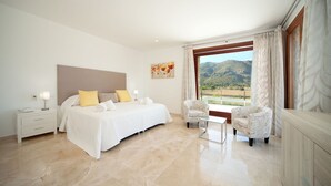 Habitación de hotel con una cama grande, una mesita de noche, una silla y vistas a las montañas.
