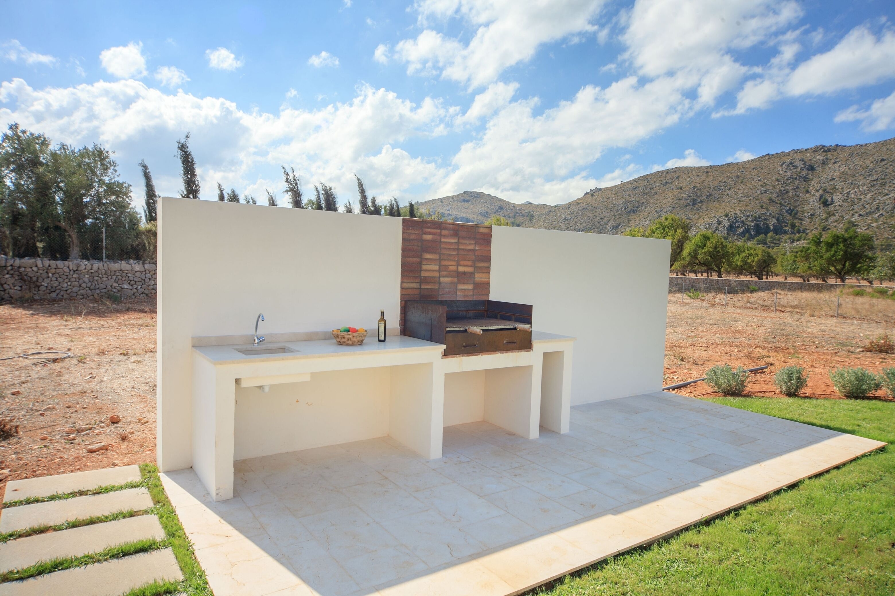 An outdoor kitchen area with a sink, a grill, and a stone wall backdrop.