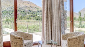 Une pièce avec deux fauteuils et une table en verre, de grandes fenêtres avec des rideaux, et une vue sur un paysage montagneux.
