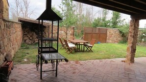 Una terrazza esterna con un muro in pietra, un tavolo e sedie in legno e una sedia a dondolo.