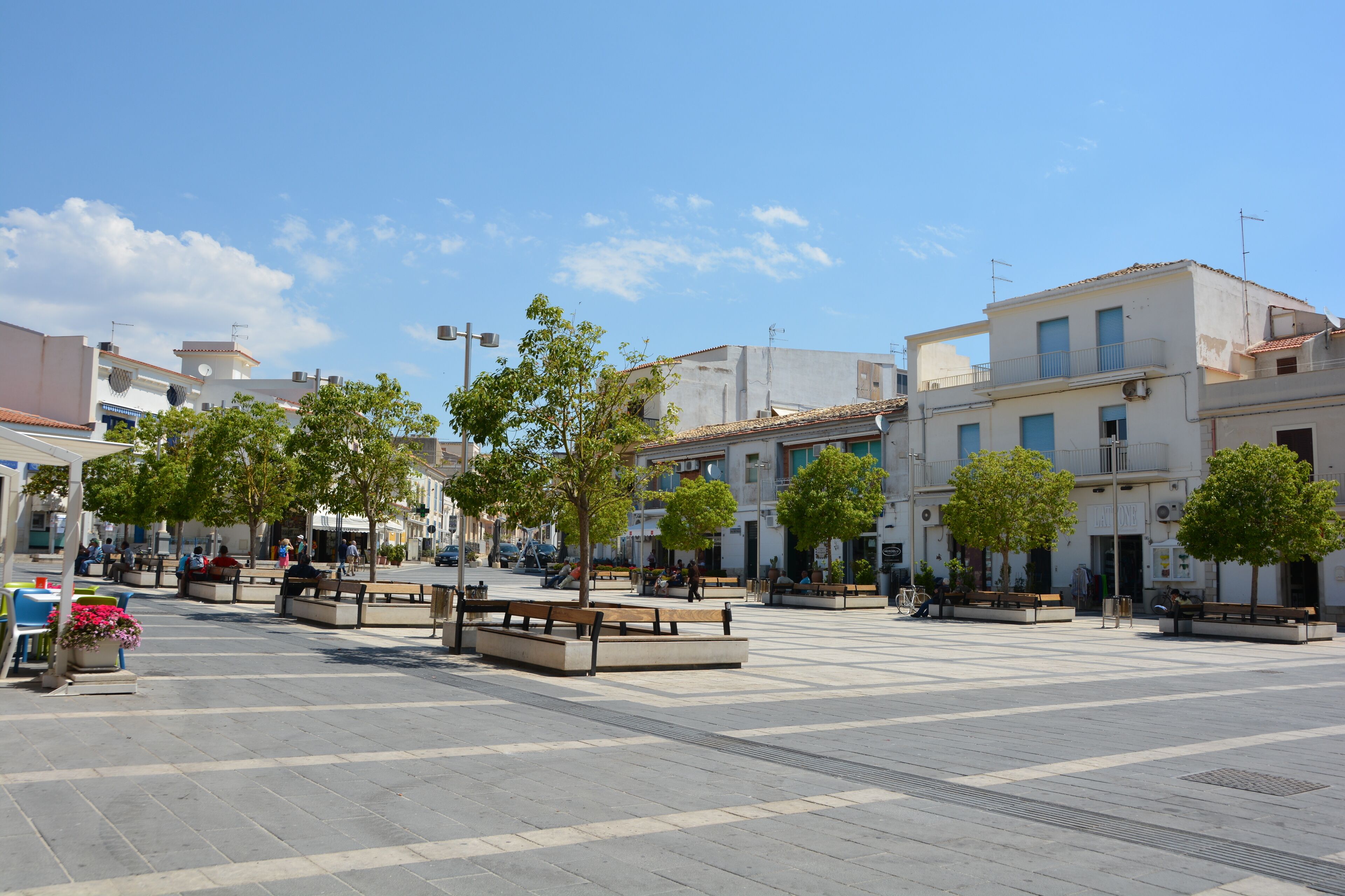 Un'ampia piazza pubblica con panchine e alberi, circondata da edifici con balconi e finestre.