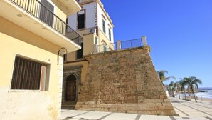 A building with a balcony, a stone wall, and a view of the beach. - Apartment 10 meters from the sea for 4 people in the center, free wi-fi (Marina di Ragusa)