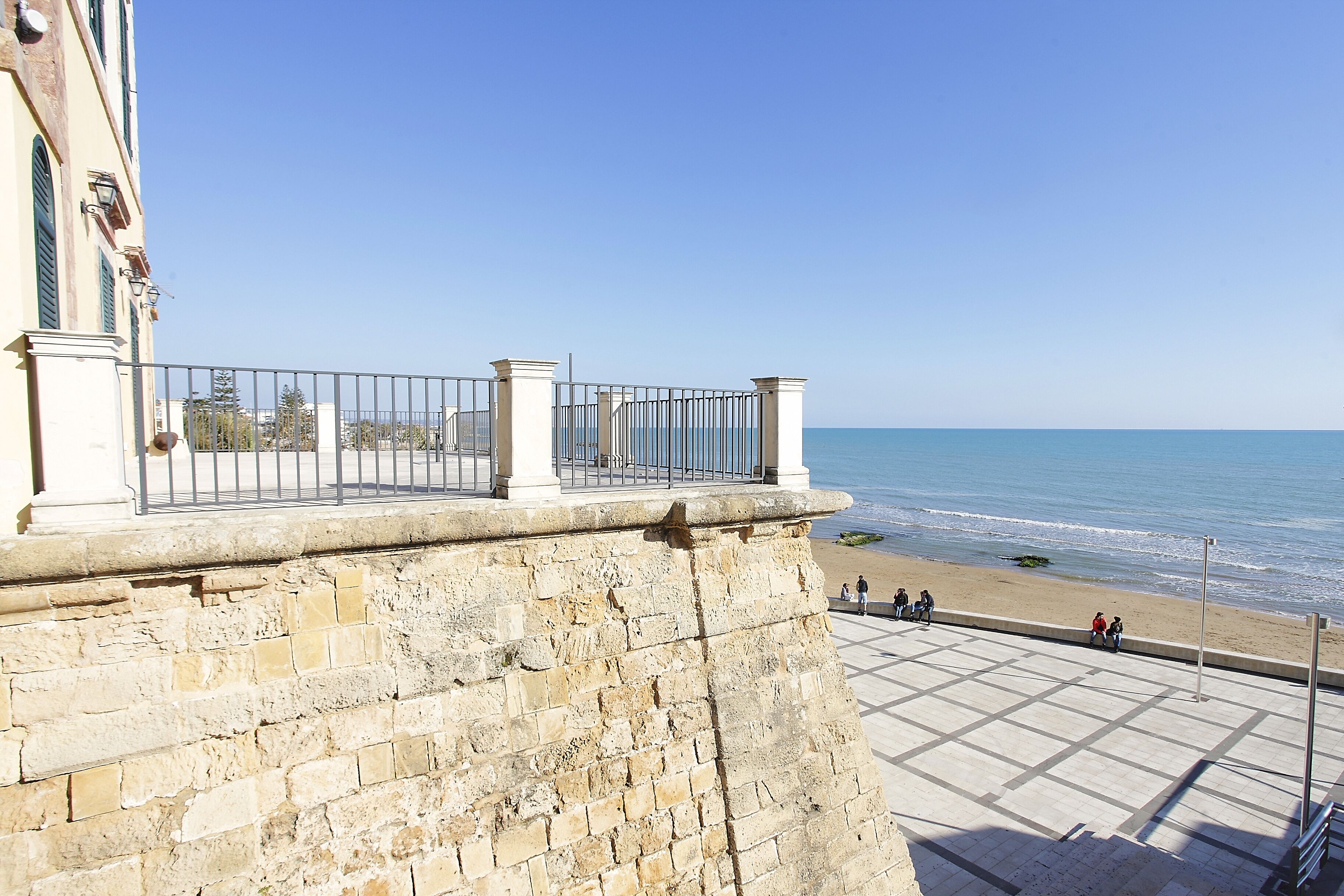 Un mur de pierre surmonté d’une rambarde métallique, donnant sur une plage.
