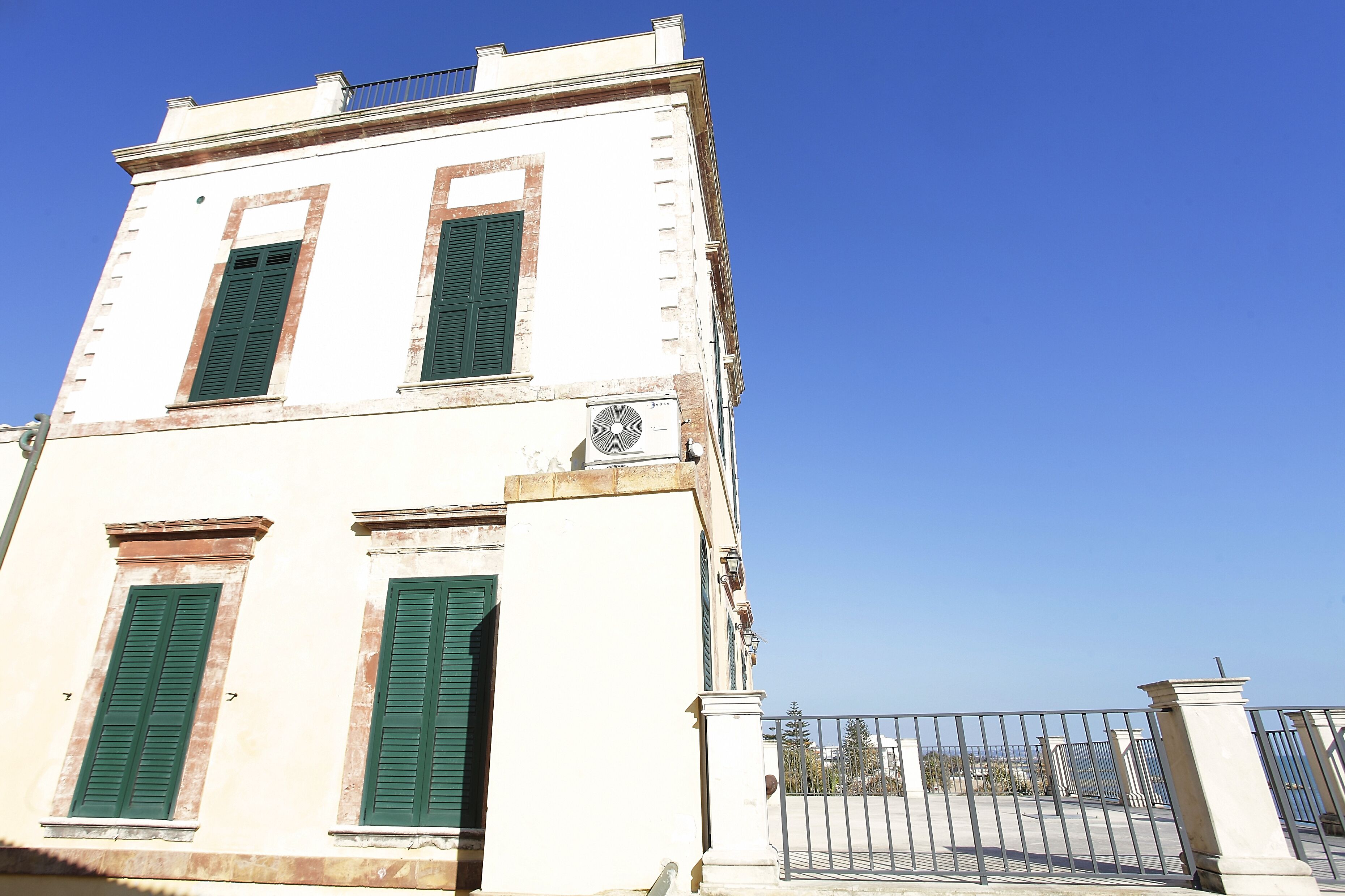 A two-story building with green shutters, a white facade, and a metal gate.